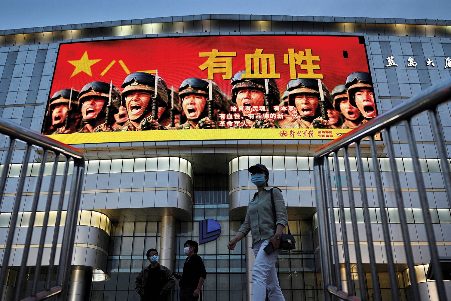 People walk past a military propaganda sign that reads “Have spirit! Raise a new generation of spirited, capable, courageous, and morally upright revolutionary soldiers” on a giant screen in Beijing.