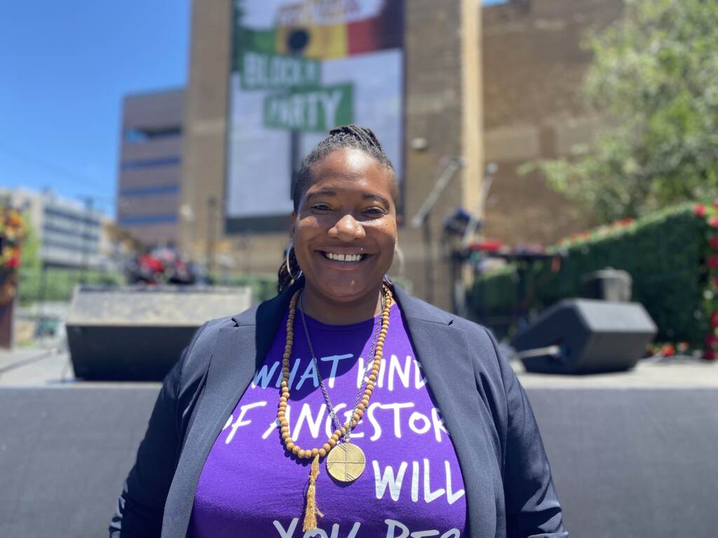 Portrait of Nina Elizabeth Ball, smiling, with a Juneteenth Block Party sign in the background.