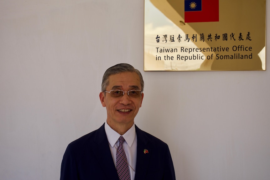 A man in a black suit stands in front of a sign that says Taiwan Representative Office